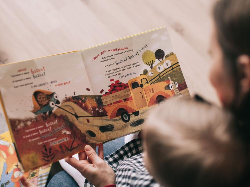 Erwachsene Hand blättert mit einem Kleinkind in einem bunten Bilderbuch