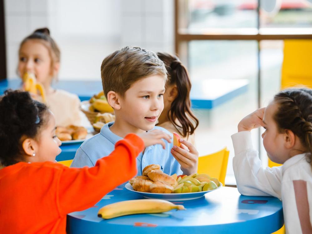Kinder sitzen gemeinsam an einem runden Tisch mit Obst und Gebäck