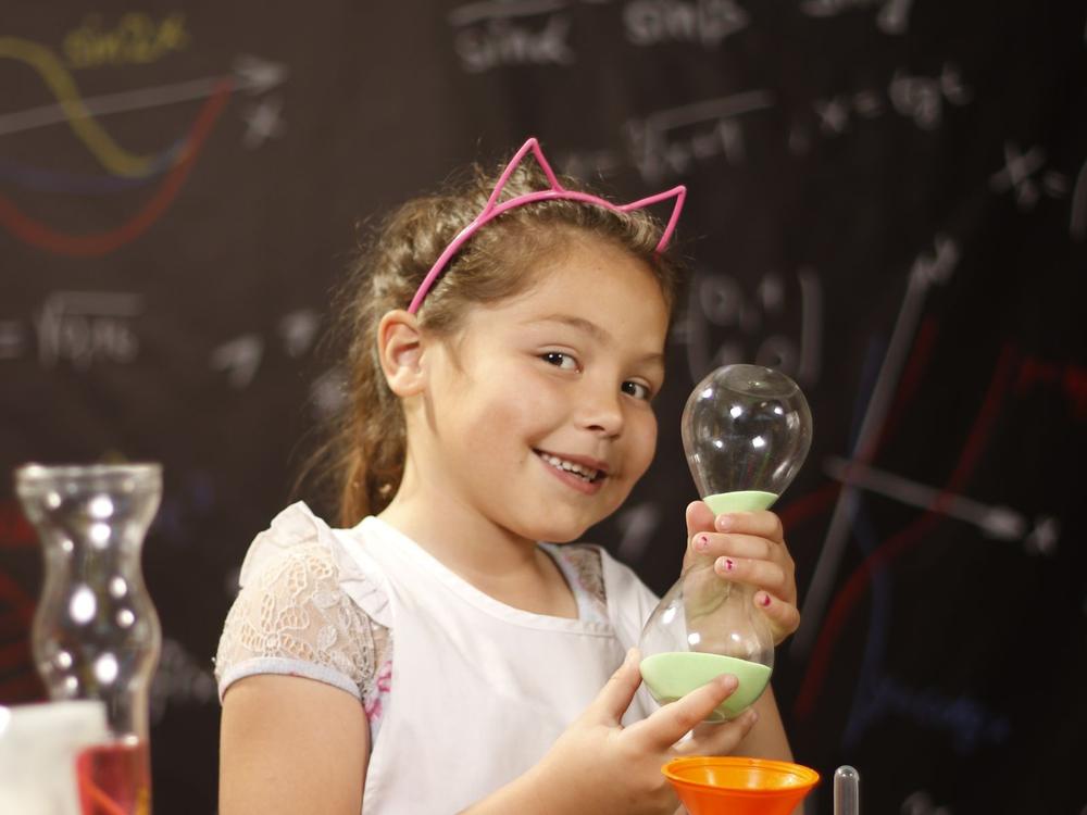 Mädchen hält lächelnd einen Glaskolben bei einem einfachen Experiment