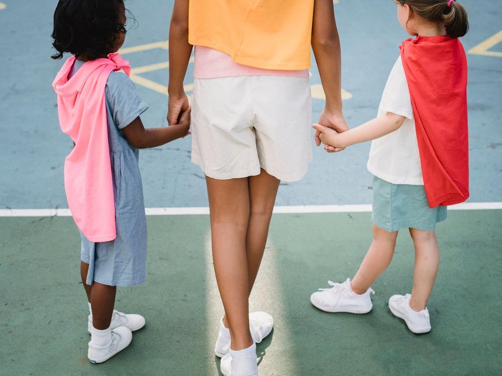 Drei Kinder halten sich an den Händen, nur Beine und Hände sind zu sehen