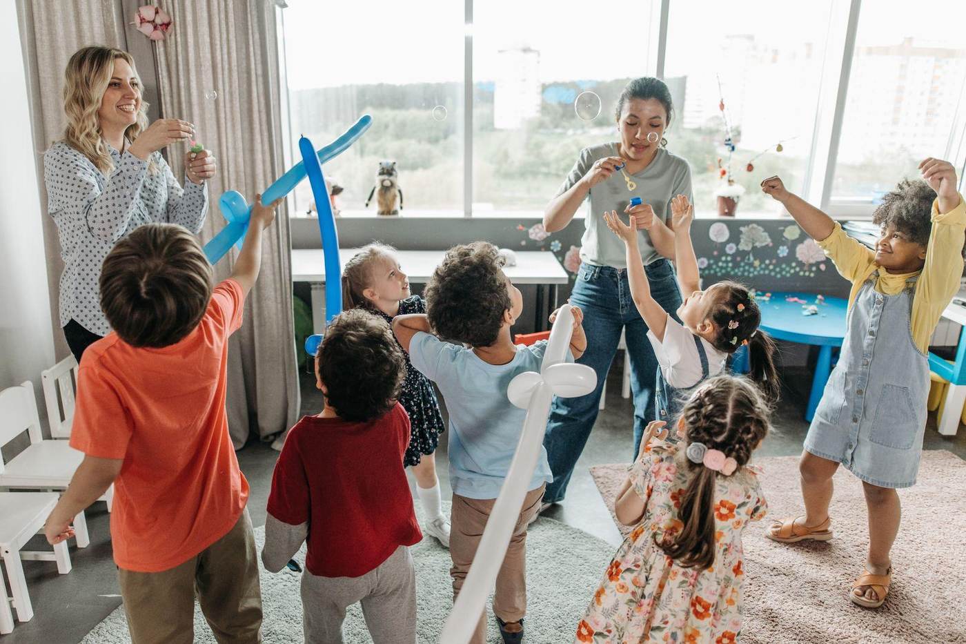 Erzieherinnen spielen mit einer fröhlichen Kindergruppe im hellen Gruppenraum