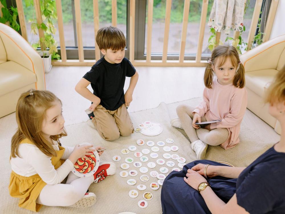 Kinder sitzen im Kreis auf dem Teppich und spielen gemeinsam ein Legespiel