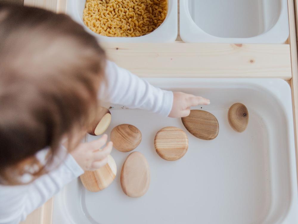 Kinderhand sortiert glatte Holzscheiben auf einem hellen Tablett