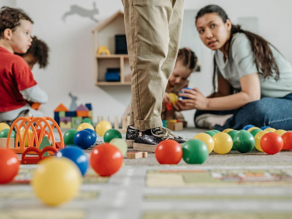 Erzieherin sitzt mit Kindern auf dem Boden zwischen bunten Spielbällen