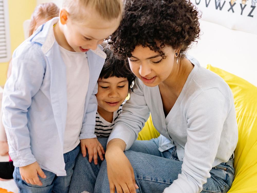 Erzieherin schaut mit zwei Kindern gemeinsam in ein Buch