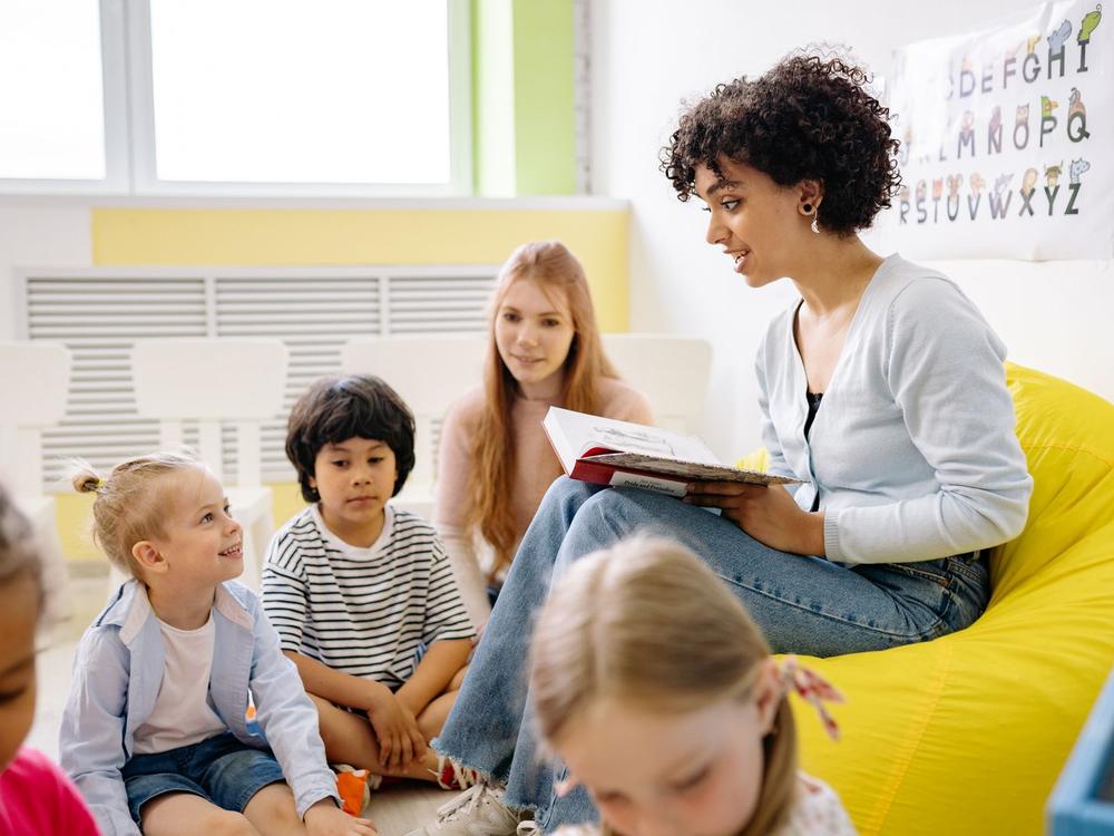Erzieherin liest einer Gruppe Kinder im Sitzkreis aus einem Bilderbuch vor