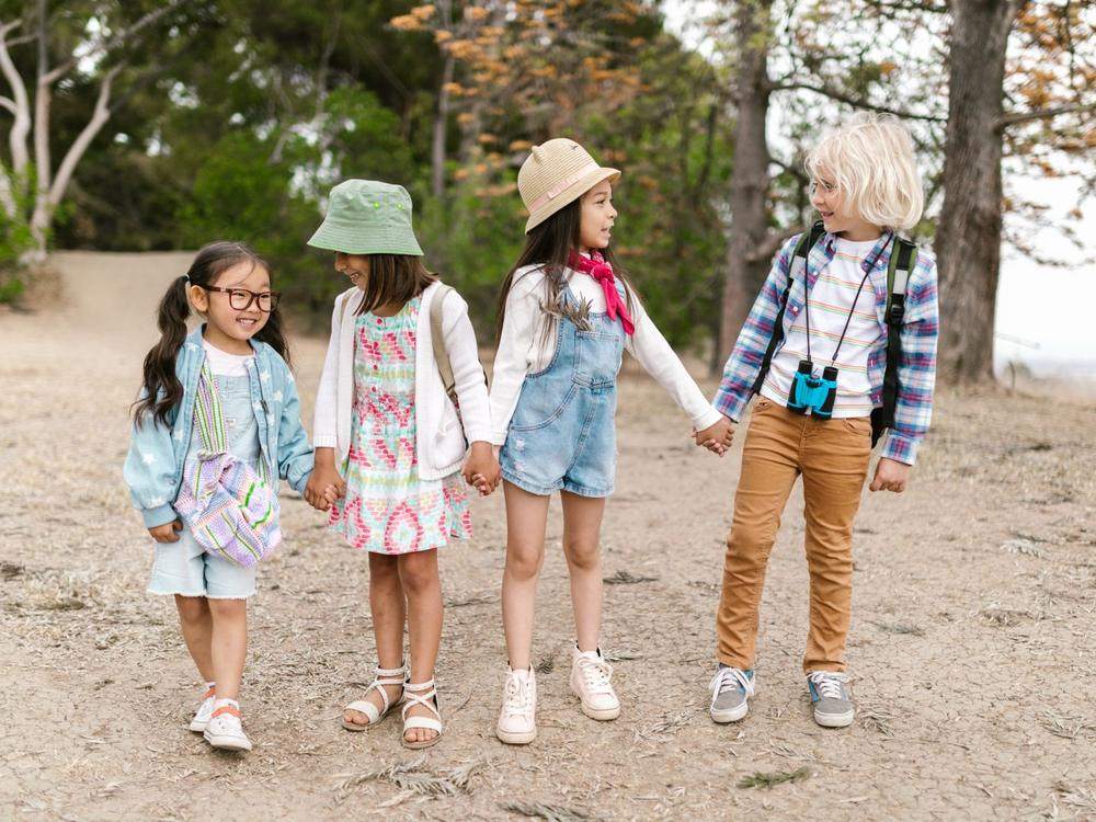 Vier Kinder unterschiedlicher Herkunft gehen Hand in Hand durch die Natur